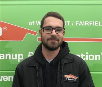 Male employee with brown hair and glasses smiling in front of green van.